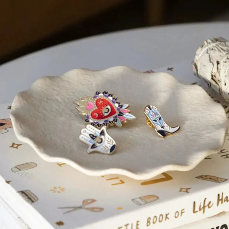 Avec humour et style, la marque All The Ways To Say arbore un design unique et décalé, toujours très coloré. Découvrez ce magnifique pin’s Fatma représentant une main bleutée avec un œil au centre dans un lotus afin d’ éloigner le mauvais œil. La marque française All The Ways To Say est une marque féminine et colorée !