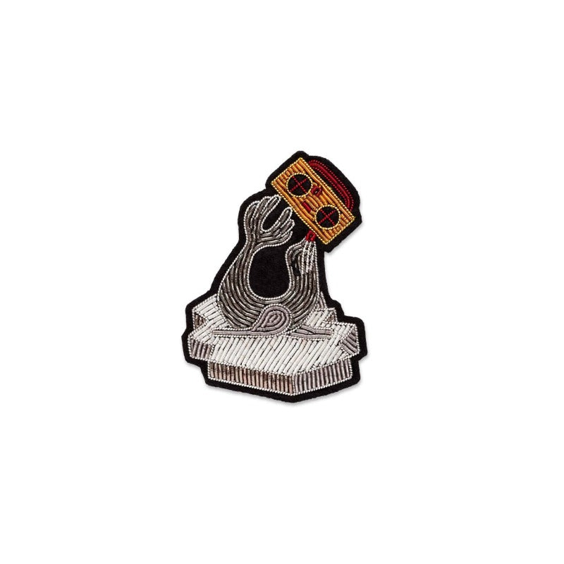 Broche brodée à la main en fil de cannetille de la marque Macon & Lesquoy. Collection Froid Automne-Hiver 2022. Broche musique de loutre. Coloris : argenté et nuances de doré et marron. Dimensions : 4,1 x 5,8 cm. broche sur fond blanc.