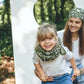 Foulard en block print avec des fleurs blanches sur fond vert ortiesde couleur vert présenté par une petite fille blonde souriant portant le foulard dans sa version grand  
