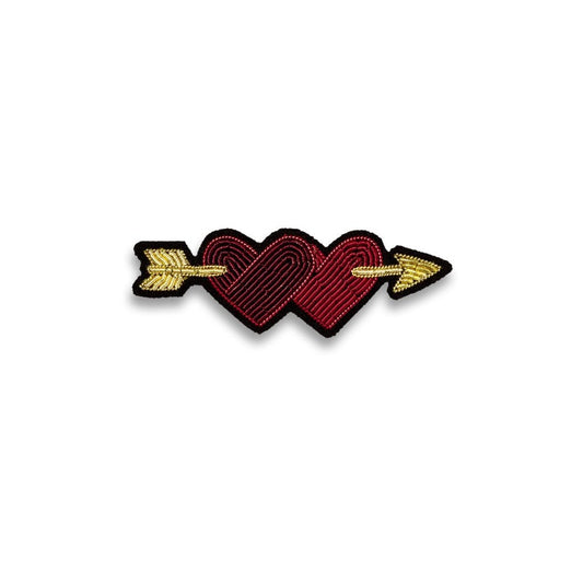 Broche brodée à la main de la marque Macon et Lesquoy. Cette broche représente deux coeurs un rouge et un bordeaux réunis par une flèche dorée