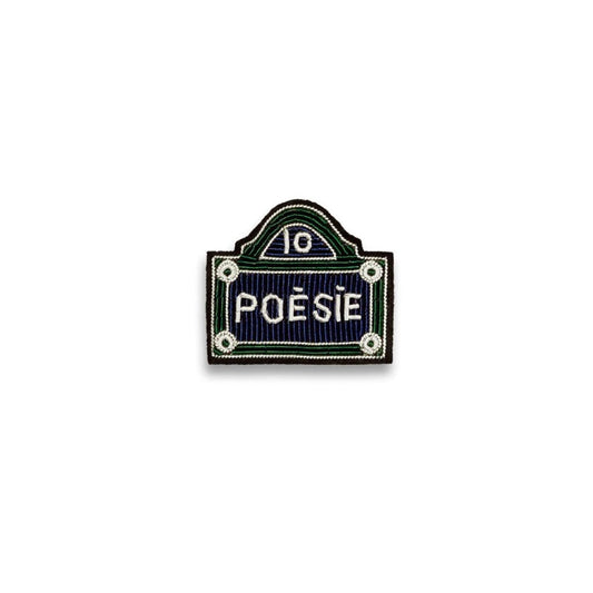 Broche brodée à la main de la marque Macon et Lesquoy. Cette broche représente une plaque de rue dénommée Poésie, de couleur, bleue, verte et blanche.