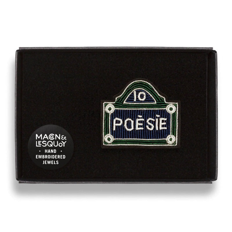 Broche brodée à la main de la marque Macon et Lesquoy. Cette broche représente une plaque de rue dénommée Poésie, de couleur, bleue, verte et blanche dans son écrin de velours.