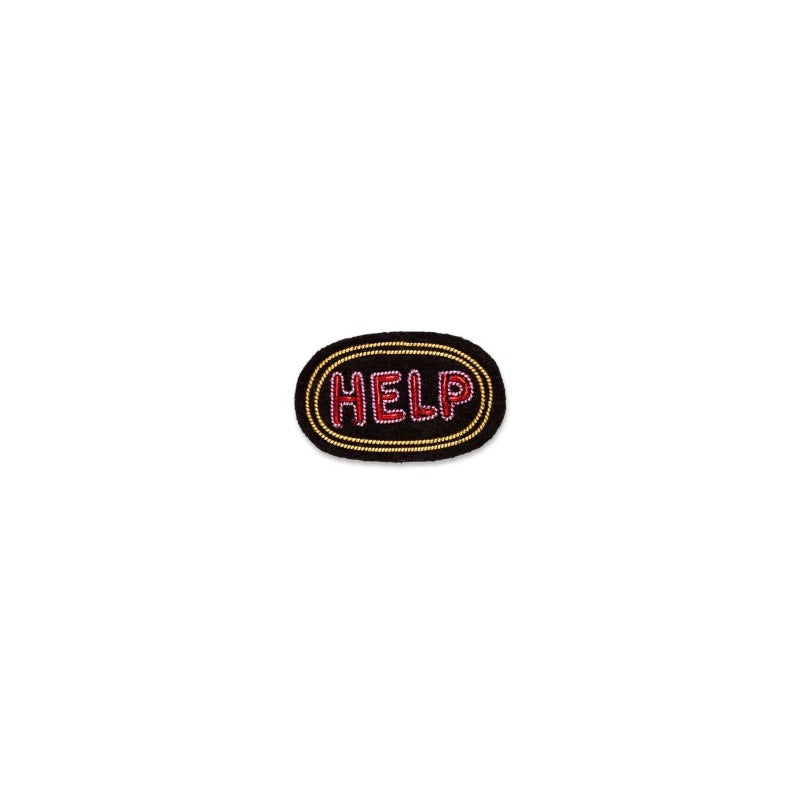 Broche brodée à la main en fil de cannetille de la marque Macon & Lesquoy. Collection Automne-Hiver 2022, modèle help, coloris doré et rouge. Dimensions : 2 x 3,3 cm. Broche sur fond blanc