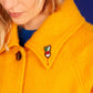 Petit radis, broche brodée à la main de Macon & Lesquoy, épinglée sur un manteau d'hiver jaune orangé